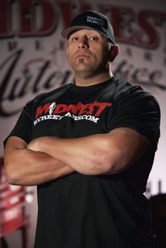 a man with his arms crossed standing in front of a sign that says one week