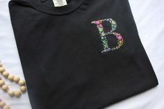 a t - shirt with the letter b embroidered on it next to beaded necklaces