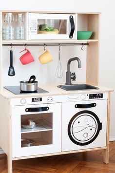 a wooden play kitchen with pots, pans and utensils on the shelves