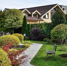 a wooden bench sitting in the middle of a lush green park next to a house