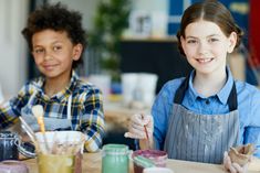 two young children sitting at a table with paint and brushes