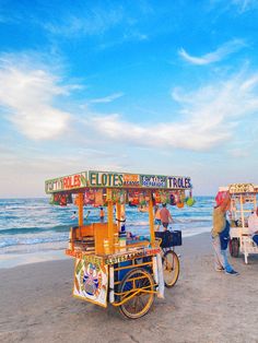 an ice cream cart on the beach with people standing around