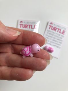 a tiny pink turtle toy sitting on top of someone's finger