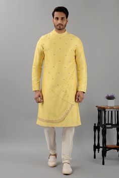 Pale yellow raw silk kurta with band collar, overlap asymmetric panels, floral pattern contrast thread and bead embroidery. Paired with white gathered churidar.
Components: 2
Pattern: Embroidered
Type Of Work: Thread and Bead Work
Neckline: Band Collar
Sleeve Type: Full Sleeves
Fabric: Raw Silk
Color: Yellow
Other Details: 
Curved panel hem
Side slits on kurta
Kurta Closure: Shoulder concealed zip
Occasion: Destination Wedding,Sangeet - Aza Fashions Ceremonial Slub Silk Traditional Wear For Eid, Fitted Yellow Raw Silk Traditional Wear, Ceremonial Traditional Wear With Resham Embroidery In Slub Silk, Festive Yellow Kurta With Pallu, Bollywood Style Ceremonial Traditional Slub Silk Wear, Yellow Kurta For Festive Occasion And Eid, Ceremonial Festive Churidar With Dori Work, Yellow Festive Kurta For Eid, Festive Yellow Kurta For Eid