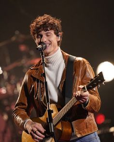 a young man holding a guitar and singing into a microphone on top of a stage