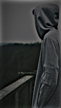 a man in a hoodie looking out over the ocean from a balcony railing with his back turned to the camera