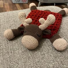 a crocheted stuffed animal laying on top of a couch next to a red pillow