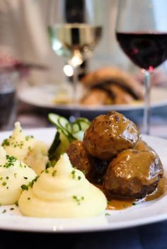 a white plate topped with meatballs and potatoes next to a glass of red wine