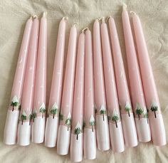 six pink candles decorated with christmas trees and stars are lined up on a white sheet