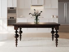 a vase with flowers on top of a wooden table in a white and beige kitchen