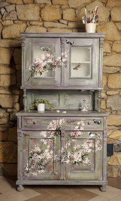 an old dresser with flowers painted on the doors and drawers is shown in front of a stone wall