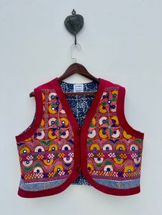 *Tribal Indian vintage hand embroidered banjara fabric/ tapestry up-cycled into a beautiful ethnic multicoloured mirror embellished waistcoat *Garment Measurements ( follow guide in the picture preferably measure your own coat and compare ) Chest: 48 inch/ 122 cm Length: 21 inch / 53cm Shoulder: 16.5 inch / 42 cm Size:  Medium /Large *One of a kind piece *Complete hand embroidered art constitites geometric pattern embroidery interspersed with big and small mirrors, the iconography is naive and rustic.  *Mirrors in the nomadic art symbolize protetive charm against evil eye. *Open sleeveless Jacket/ waistcoat ( with block printed cotton lining inside) *The jacket you will recieve will be exact one as the picture. *Dry Clean only Please Note: Due to use of Vintage fabric almost 40- 50 years o Embroidered Bohemian Choli For Summer, Summer Bohemian Embroidered Choli, Summer Festival Embroidered Choli, Fitted Bohemian Vest For Festive Occasions, Festive Bohemian Vest With Floral Embroidery, Summer Bohemian Choli With Motifs, Multicolor Hippie Festival Vest, Bohemian Style Summer Festive Choli, Bohemian Summer Festive Choli