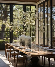 a dining room table with vases and glasses on it in front of large windows