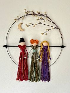 three dolls are hanging on a circular wall decoration with branches and moon in the background