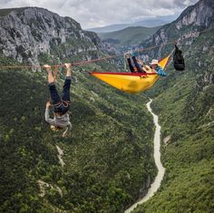 two people hanging upside down in the middle of a valley with a river running through it