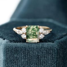 a close up of a ring on top of a blue velvet box with a green and white stone in the middle