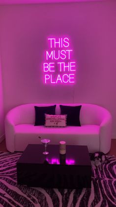 a living room with a white couch and pink neon sign on the wall above it