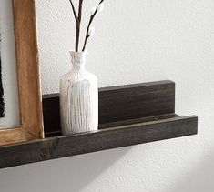 a white vase sitting on top of a wooden shelf next to a framed photo and flowers