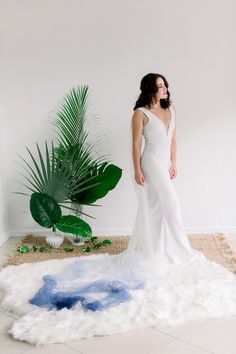 a woman in a white dress standing on a rug next to a potted plant