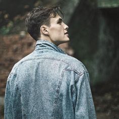 a young man wearing a jean jacket looking off into the distance