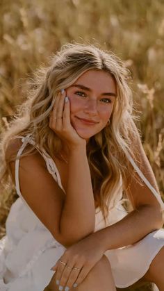 a woman sitting in the grass with her hand on her face and looking at the camera