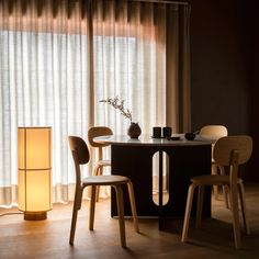 a table with chairs and a lamp in front of it on a wooden floor next to a window