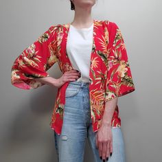 a woman standing in front of a gray wall wearing a red and yellow floral jacket