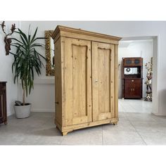 a large wooden armoire sitting in the middle of a room next to a potted plant