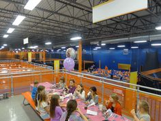 several children sitting at tables in an indoor area with orange walls and metal railings