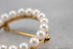 This vintage pearl circle brooch is a true classic! Simple and refined, traditional white pearls form a shimmering wreath, backed by rich yellow gold. This brooch would look wonderful pinned to a scarf or lapel, or even on a bridal bouquet! Love this piece but want to make it more versatile? We here at Market Square Jewelers, along with our master metalsmiths can convert this fantastic brooch into a necklace or pendant for an additional fee. Please contact us for more information! Metal: 10K Yel Timeless Wedding Brooch Jewelry, Classic Gold Round Brooches, Classic Round Jewelry Brooch, Elegant Yellow Gold Round Brooches, Classic Yellow Gold Brooches For Wedding, Classic Yellow Gold Round Brooches, Classic Round Yellow Gold Brooches, Classic Yellow Gold Wedding Brooches, Jewelry Bouquet