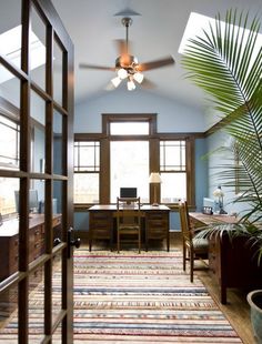 a room with a ceiling fan and rug on the floor next to a desk in front of a window