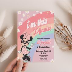 a person holding up a minnie mouse birthday party card in front of flowers and feathers