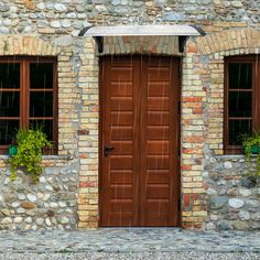 an old brick building with two brown doors and three planters on the windows sill