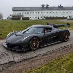 a black sports car driving down a road next to a large white building on a foggy day