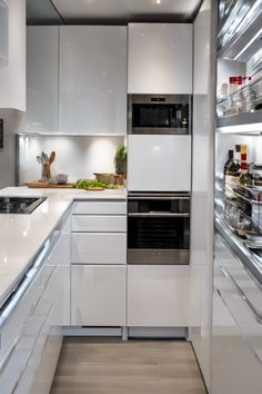 Modern kitchen with sleek white cabinets, built-in appliances, and open shelves stocked with jars and bottles.