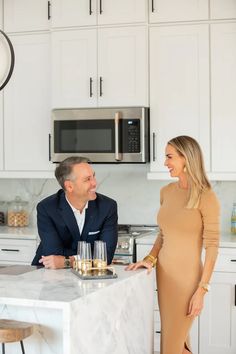 a man and woman standing in a kitchen next to a counter with wine glasses on it