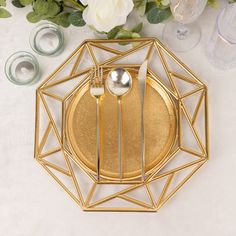 a gold plate with two silver spoons on it next to some white flowers and candles