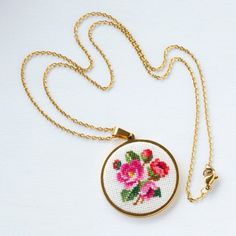 a cross - stitch necklace with flowers on it is hanging from a gold plated chain