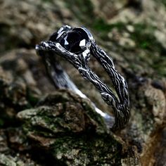 a black diamond ring sitting on top of a moss covered tree branch in front of a rock