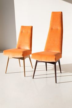 two orange chairs sitting next to each other on top of a white floor in front of a wall