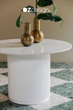 two gold vases sitting on top of a white table with green plants in it