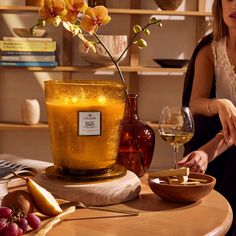 a woman sitting at a table with a glass of wine in front of her and a vase filled with flowers