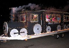 a train with lights on the side and people in it's windows is being transported by a trailer