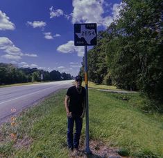 a man standing next to a street sign on the side of a road with trees in the background