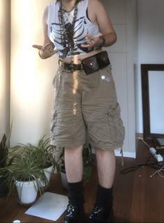 A mid-sized person/girl wearing cropped white rib cage t-shirt,  wide light brown cargo shorts, dark brown legwarmers, black platform dr. Martens and multiple crystal rings and bracelets. 		The person is also wearing multiple silver necklaces. Jorts Outfit Idea Alt, Masc Grunge Outfits Summer, Gremlincore Outfits Summer, Crowcore Diy, Summer Outfits Punk, Earth Tone Summer Outfits, Punk Outfits Summer, Grunge Outfit Summer, Summer Punk Outfits