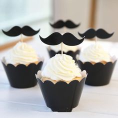 cupcakes with white frosting and black moustaches are on the table