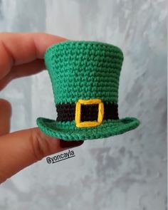 a crocheted green hat with a yellow buckle is held up to the camera