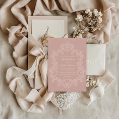 the wedding stationery is laid out on top of some fabric and lace, along with flowers