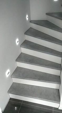 a set of stairs with lights on each step in a room that has white walls and black tile flooring