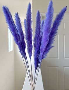 three purple flowers in a green vase on a table next to a white wall and door